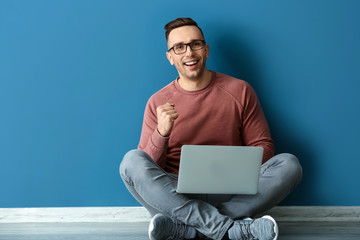 Successful young man with laptop sitting near color wall