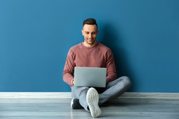 Young man with laptop sitting near color wall