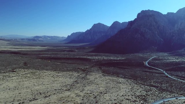 A drone shot of a curved road in the middle of a beautiful valley surrounded by high mountains