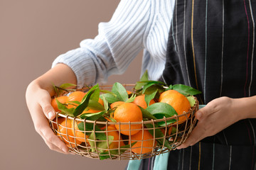 Woman holding basket with tasty tangerines on color background, closeup