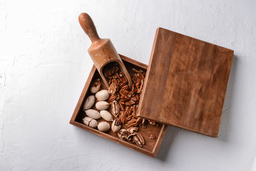 Scoop and box with pecan nuts on light background