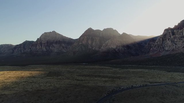 An aerial shot of a curved road leading through a valley between tall mountains in the light of a stunning sunrise
