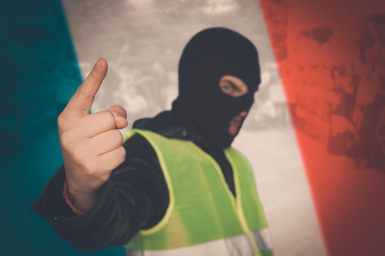 Concept Of Street Protests Of Workers, Proletarians Against System, Bourgeoisie. Yellow Vests Protest Against Higher Fuel Prices In France. Man In A Mask And A Yellow Vest On Background Of French Flag