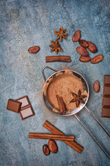 Cocoa powder in strainer with pieces of chocolate bars and spices as ingredients for confectionery
