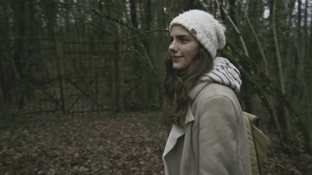 close shot of a girl walking on a grass and mud track in a french forest and reach an old destroyed military gate