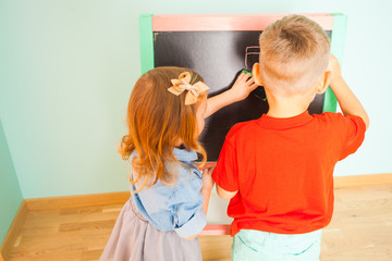 Little preschoolers writing on black board indoors