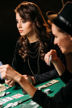 beautiful women playing poker with cards and chips at table in casino