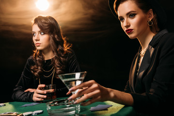 attractive girls playing poker at table in casino, woman holding glass of cocktail