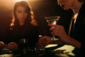 cropped image of attractive girls playing poker at table in casino, woman holding glass of cocktail