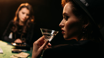 Plakat attractive girl drinking cocktail while playing poker at table in casino
