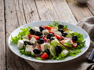 Greek salad on white plate on old rustic wooden table, side view, copy space