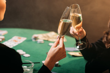 cropped image of girls clinking with glasses of champagne at poker table in casino
