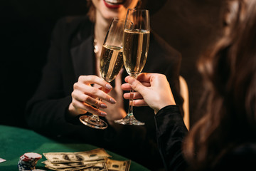 cropped image of happy girls clinking with glasses of champagne at poker table in casino
