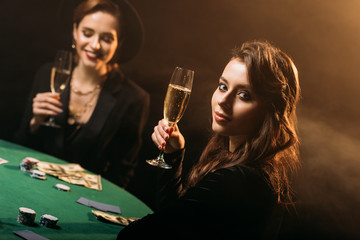 attractive girls holding glasses of champagne at poker table in casino