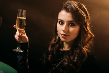 attractive girl holding glass of champagne and looking at camera on brown