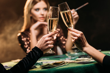 selective focus of attractive girls clinking with glasses of champagne at poker table in casino