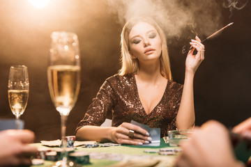 selective focus of attractive girl smoking cigarette at poker table in casino - obrazy, fototapety, plakaty