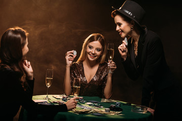 attractive smiling girls looking at each other at poker table in casino