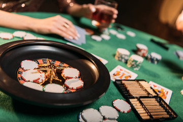 cropped image of girl playing poker at table in casino, roulette and cigars on foreground