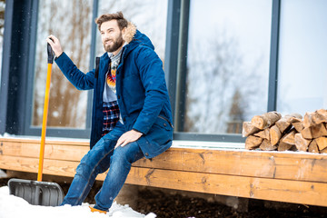 Portrait of a handsome man in winter clothes sitting on the terrace of the modern house