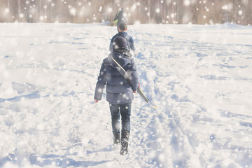 Two teen boys walk with ski in the park in the winter snowfall. Concept of friendships