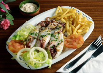 Plato combinado en una bandeja con tres calamares a la plancha, patatas fritas y ensalada.