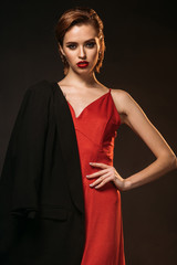 beautiful woman in red dress and black jacket on one shoulder looking at camera isolated on black