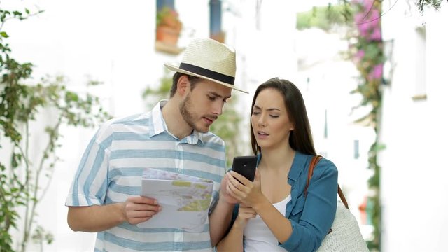 Front view of two happy tourists walking checking smart phone content on vacation