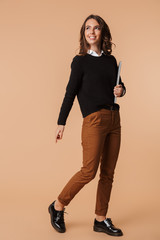 Photo of young woman 20s walking and holding laptop, isolated over beige background