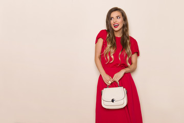 Fototapeta na wymiar Smiling Beautiful Woman In Red Dress With Beige Purse Is Looking Away And Talking