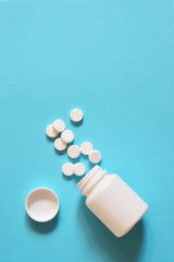 white pills scattered on a blue background. pills spilled out of the bottle. copy space for text