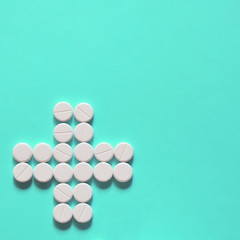 white pills laid out in the shape of a cross on a blue background. copy space for text