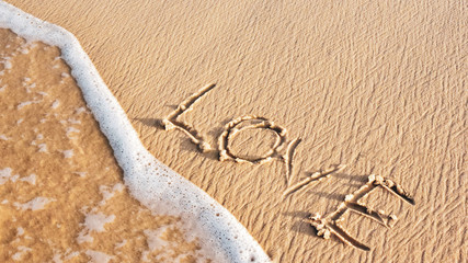 inscription LOVE on the sand of the beach. wave on the shore