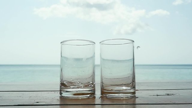 Water is poured into a glasses against the sea on tropical beach. slow motion. 1920x1080