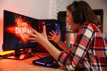 Angry girl gamer sitting at the table, playing online games © Drobot Dean