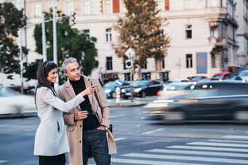 Man and woman business partners crossing road outdoors in city, talking.