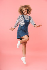 Full length image of amusing curly woman 20s wearing casual clothes smiling while, isolated over pink background