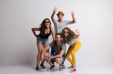 Portrait of joyful young group of friends with hat and sunglasses standing in a studio.