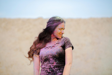 Pretty brunette woman with long curly hair wearing black t shirt covered with colorful dry paint Holi at the desert