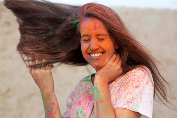 Joyful young woman with wind in hair celebrating Holi colors festival at the desert