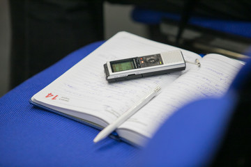 Dictaphone with headphones on a light worktable of a journalist with a notebook, a green succulent and a laptop. In the sunlight