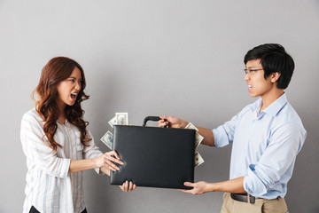 Angry asian couple standing isolated over gray