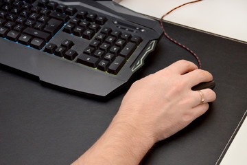 Guy is playing a video game. Close up of a hand lying on a mouse and a black gaming keyboard on a black table. Top view.
