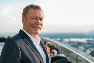 Happy senior businessman with mustache smiling against view of the city