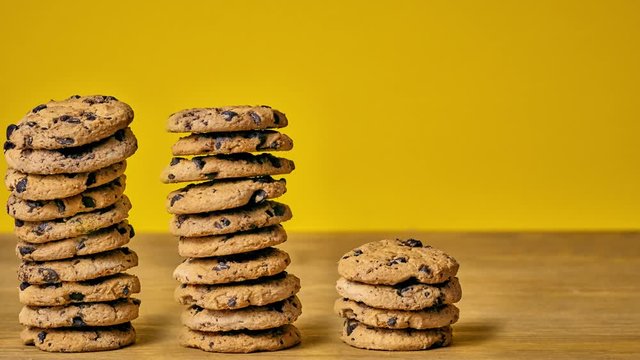 Homemade chocolate cookies are piled on a wooden table, yellow background