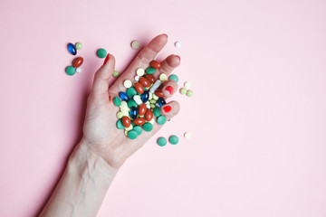 female hands and colorful pills, tablets, capsules on pink background, top view, flat lay