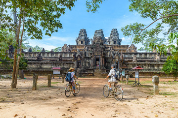 Fototapeta premium Tourist couple cycling around Angkor temple, Cambodia. Ta Keo building ruins in the jungle. Eco friendly tourism traveling.