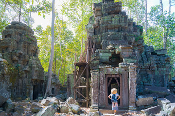 One tourist visiting Angkor ruins amid jungle, Ta Nei temple, travel destination Cambodia. Woman with traditional hat, rear view.