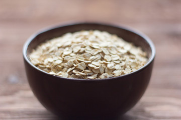 oat flakes, oat in dark bowl on wooden background