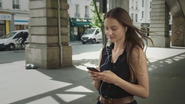 Woman goes out for a walk to relax in the city of Paris while listening to music on her phone